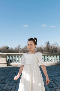 A young girl enjoys a sunny day outdoors, dressed in a beautiful white First Communion dress. The