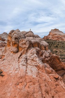 Unrecognizable explorer standing atop a unique swirling rock formation in White Pocket, Arizona,