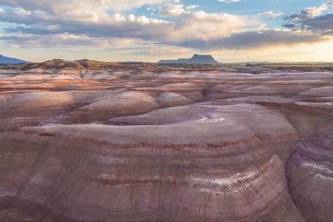 Majestic aerial view of striated Bentonite hills under a vast sky in Utah, showcasing the stunning
