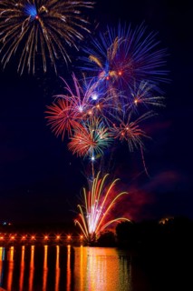 Vibrant fireworks illuminate the night sky above the Ebro River, reflecting on its calm waters. The
