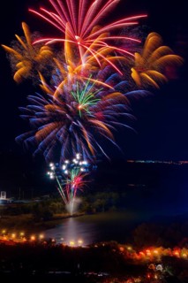 Vibrant fireworks illuminate the night sky above the Ebro River, casting colorful reflections on