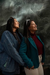 A joyful Latin lesbian couple shares a heartfelt moment, smiling warmly. They are dressed