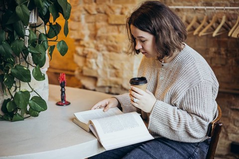 A young woman enjoys reading a book in a cozy bookstore setting She is sipping coffee, surrounded