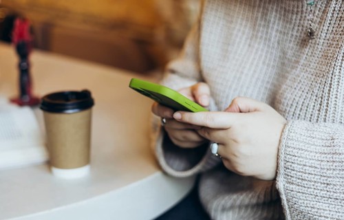 Close-up of a woman's hands holding a green smartphone in a bookstore cafe A takeaway coffee cup