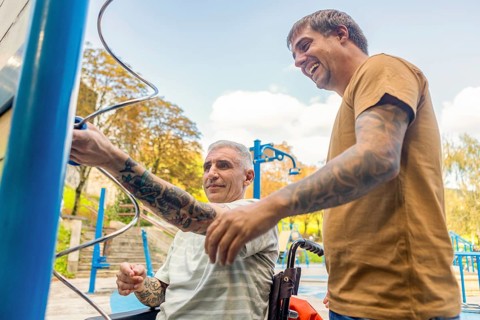 Two friends, one in a wheelchair by cerebral palsy, enjoy a sunny day at an inclusive park,