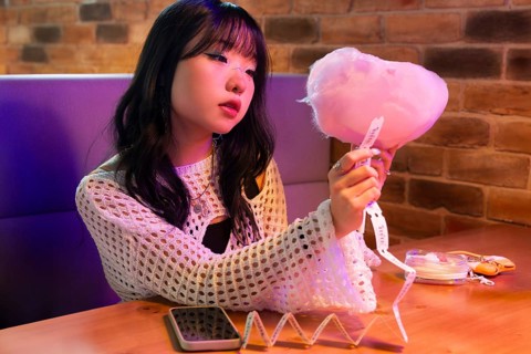 Young Asian Gen Z girl enjoys a vibrant arcade environment, sitting at a colorful booth with cotton