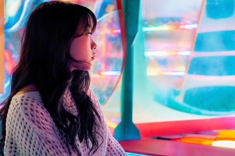 A young Asian Gen Z girl enjoys vivid lights and colors in an arcade, capturing the essence of
