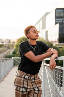 Young latin transgender with short hair and sunglasses, leaning casually against a railing in an