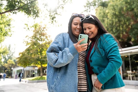 A joyous latin lesbian couple is seen sharing a heartwarming moment outdoors, smiling at a phone
