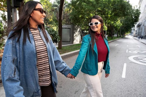 A joyful latin lesbian couple walks hand in hand down a sunlit city street, exuding happiness and
