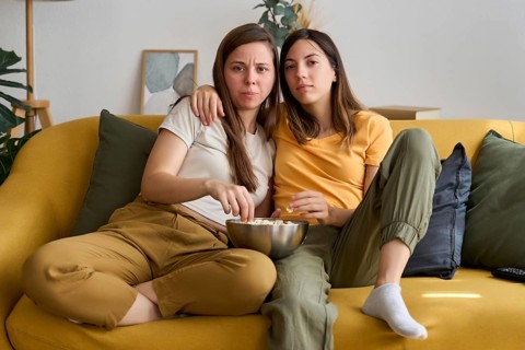 A loving lesbian couple is sitting on a comfortable sofa, enjoying a movie night with popcorn Their
