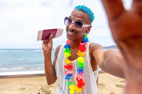 LGBTQIA+ man with colorful accessories joyfully preparing for a summer holiday. Beach scene evokes