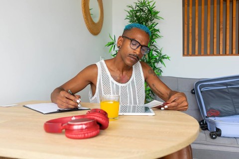 LGBTQIA+ person meticulously preparing for the holidays, planning with a notebook and tablet. A