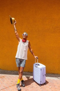 LGBTQIA+ man joyfully preparing for a holiday, standing with a suitcase against a vibrant orange