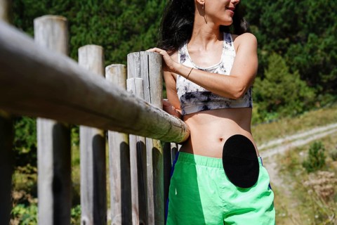 A woman with a visible ostomy bag stands confidently in a serene outdoor setting She wears a sports