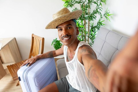 A cheerful LGBTQIA+ individual with a suitcase, ready for holiday adventures. Wearing a straw hat