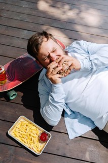 A person enjoys a barbecue meal outdoors, lying beside a skateboard. The scene includes fries with
