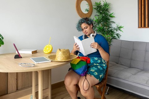 A transgender man, sitting comfortably in a modern styled room. He is deeply engaged in reading a