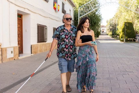 A blind father, utilizing a white cane, walks confidently through a town, guided by his attentive