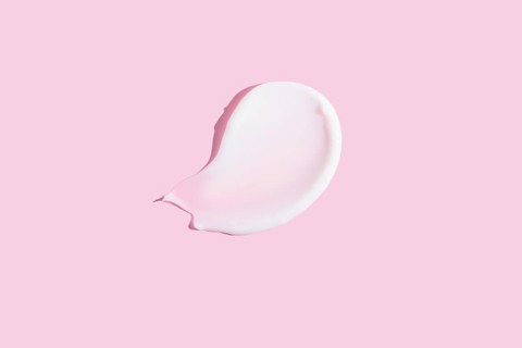 A high-quality image featuring a dollop of cosmetic cream smeared on a pastel pink background,