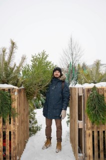 A man dressed warmly in a blue coat and gloves holds a fresh Christmas fir Snowflakes fall gently,