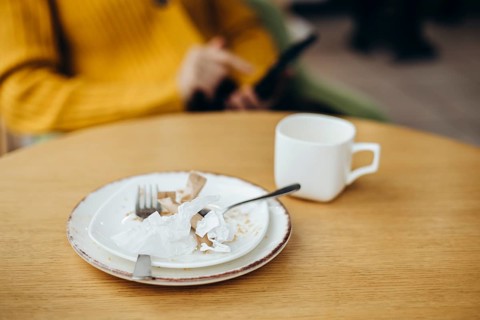 A cozy coffee shop setting featuring a wooden table with a used cup and plate Crumpled paper