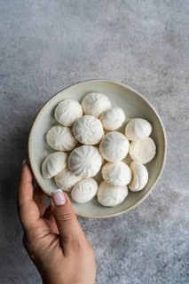A hand holding a small ceramic bowl filled with handmade mini zephyr marshmallows, highlighting