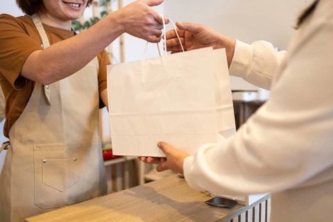 A friendly store employee hands a paper shopping bag to a customer The image captures a moment of