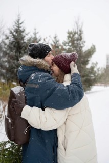 A man lovingly kisses a woman on the forehead as they embrace in a snowy park Dressed in winter