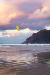 A kite surfer glides across the waves at Famara Beach, Lanzarote, under a sky painted with stunning
