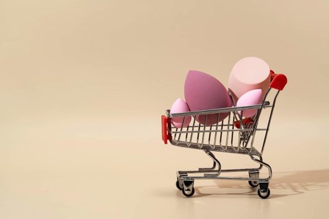 A collection of vibrant cosmetic sponges displayed in a miniature shopping cart against a soft