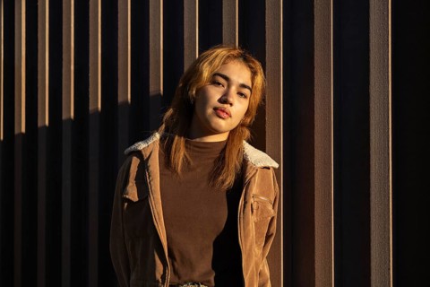 A Mixed-race woman leans against a textured wall, bathed in warm sunlight Her casual outfit and