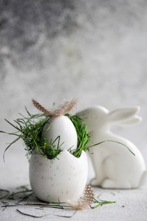 A meticulously crafted Easter setting featuring a white speckled egg cradling a nest of fresh green