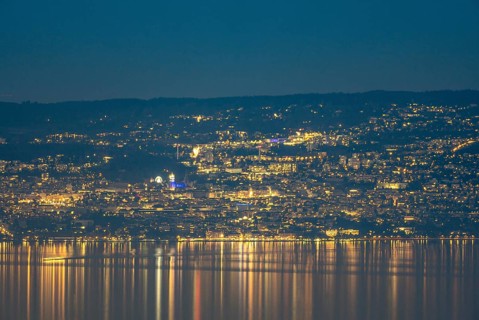 A captivating nighttime view of Lausanne, Switzerland, with the city lights reflecting on the calm