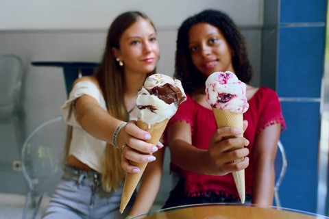 Two teenage friends, a Caucasian girl and an African girl, happily holding and showcasing their ice