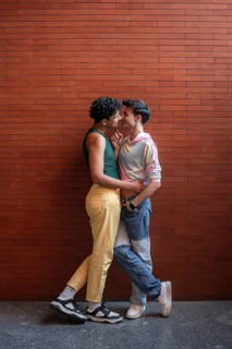 A young gay couple shares an intimate moment against a brick wall, expressing affection and love.