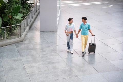 A joyful gay couple walks hand in hand through an airport terminal with luggage, enjoying each