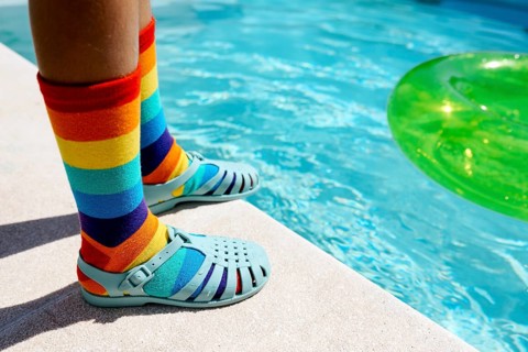 A vibrant scene featuring rainbow-striped socks paired with blue sandals by a bright swimming pool.