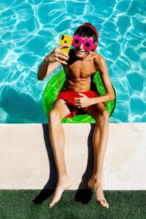 A young teenage boy relaxes on a float in a bright blue pool, wearing colorful flower-shaped