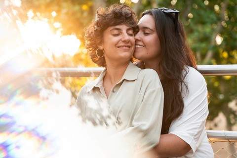 A loving lesbian couple shares a tender embrace outdoors, surrounded by vibrant nature. The