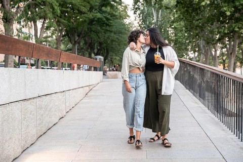 A lesbian couple shares a tender kiss while walking down a city street, displaying affection and