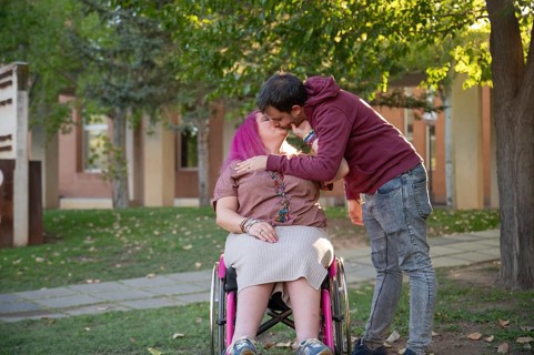 A couple shares an affectionate kiss on a peaceful college campus The woman, with pink hair and