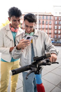 A happy gay couple, each wearing headphones, enjoys a light-hearted moment outdoors while looking