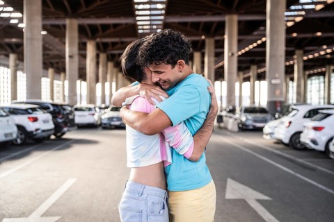 A joyful gay couple shares an embrace in a spacious urban parking garage, surrounded by parked cars