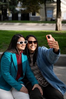 A smiling Latin lesbian couple enjoys a sunny day at the park, embracing while taking a selfie with