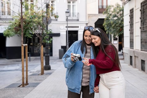 A happy latin lesbian couple enjoys a day out, capturing memories with a camera. They share a