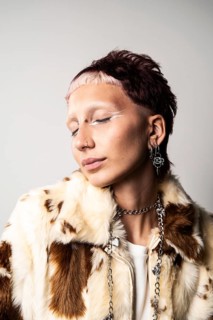 Close-up of a woman with a bold hairstyle, glamorous nose and ear piercings, striking white