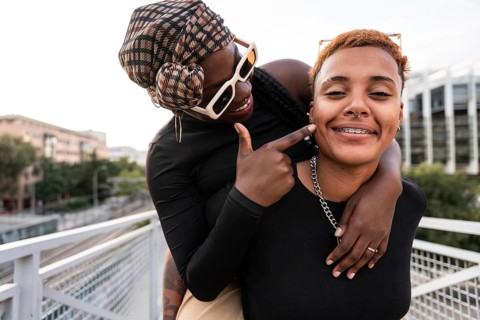 A vibrant LGBT multiethnic couple shares a joyful embrace on a sunny day outdoors, capturing a