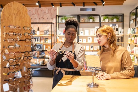 A retail employee helps a customer choose eyeglasses in a stylish boutique. The modern store is