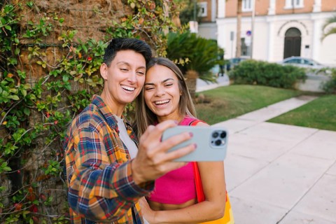 A joyful lesbian couple takes a selfie while enjoying a sunny day in a park. Their smiles reflect